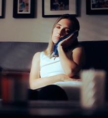 Woman on couch with eyes closed holding ice pack against face