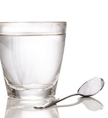 Spoonful of salt next to glass of water on reflective surface
