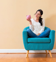 Woman in an armchair smiling at her pink piggy bank