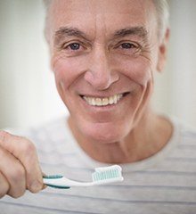 Older gentleman brushing his dentures in Farmington