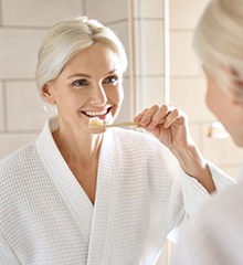 Older woman brushing teeth in front of mirror