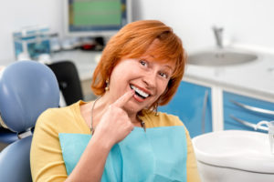 Senior woman in dental chair pointing to smile