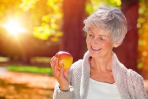 Smiling woman with dentures in Farmington holding an apple