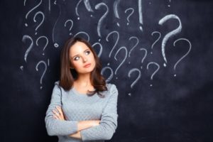 confused woman in front of a chalkboard filled with question marks 