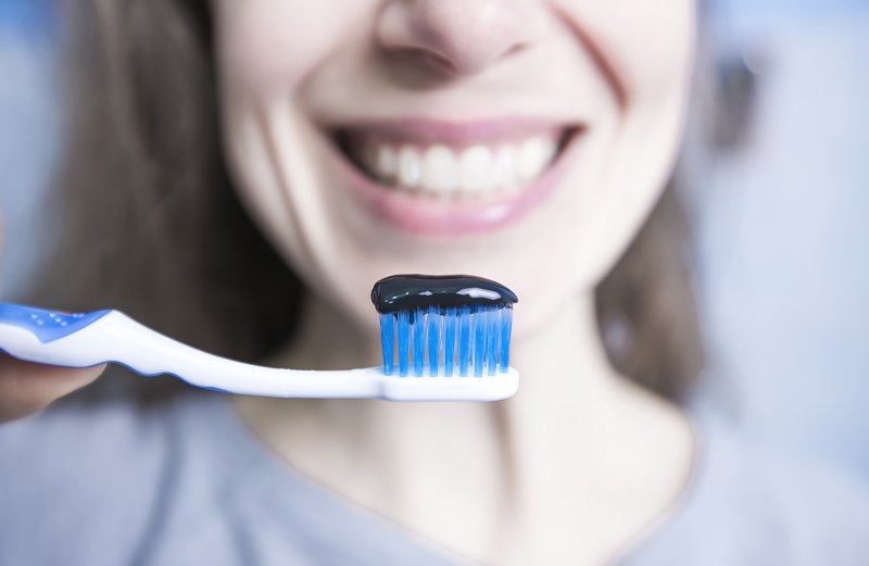 young woman holding toothbrush with charcoal toothpaste
