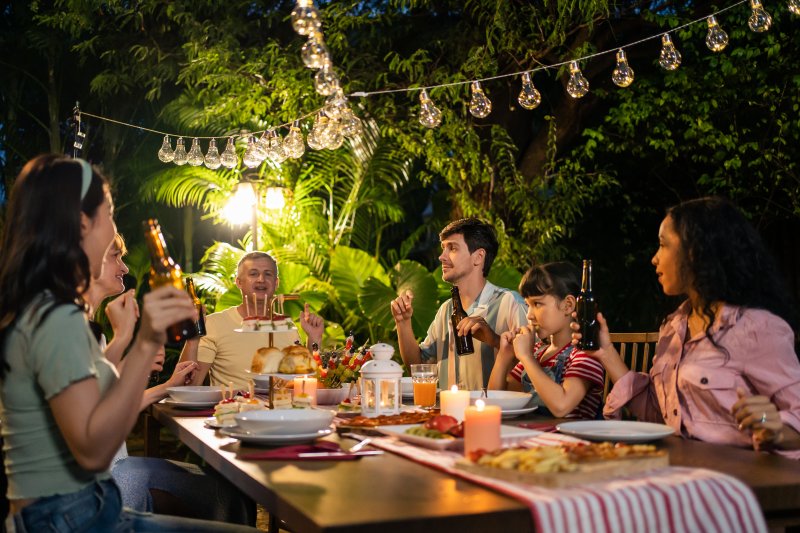 Nighttime celebration at a long rectangular table between a group of people underneath string lights with a spread of food