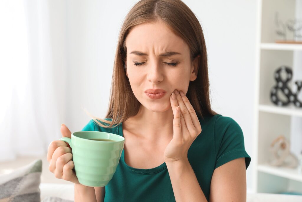 Woman drinking coffee holding fingers to cheek in pain