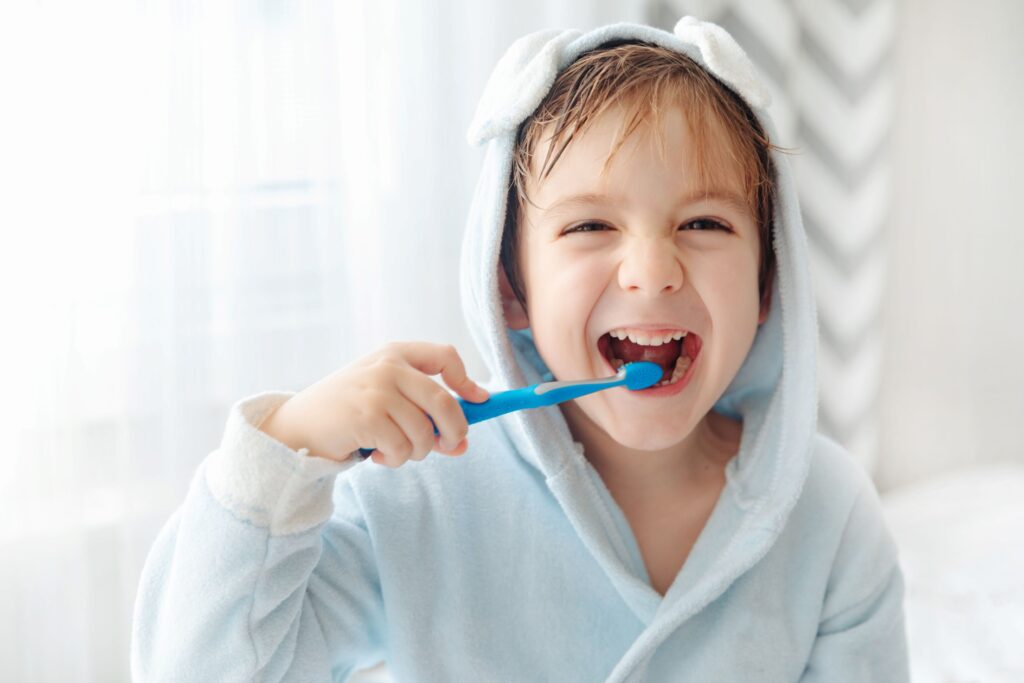 Little boy in hooded towel brushing teeth